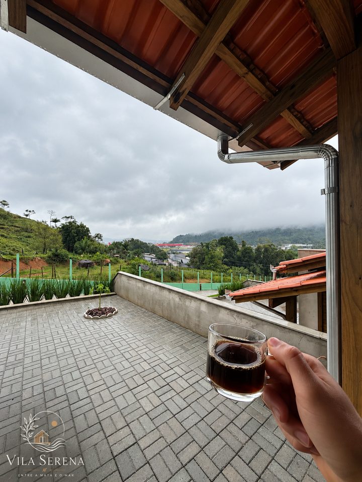 Xícara de café na varanda com vista para os morros e as casas da Vila