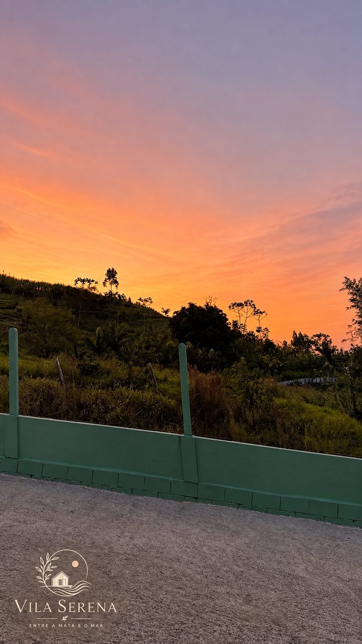 Pôr do sol laranja sobre os morros, visto da entrada da Vila